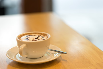 A cup of coffee with maple leaf latte art on the light brown table with blurred background