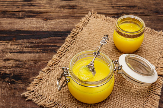 Pure or desi ghee (ghi), clarified melted butter. Healthy fats bulletproof diet concept or paleo style plan. Glass jar, silver spoon on vintage sackcloth. Wooden boards background