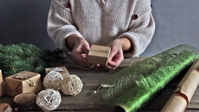 Christmas and zero waste, eco friendly packaging. Woman is wrapping gifts in craft paper on a wooden table, ecological Christmas holiday concept, eco decor