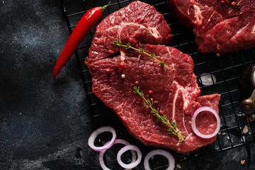 Two Raw beef steak with spices, onions and chili on dark slate or concrete background. Top view
