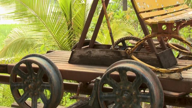 A closeup shot with an upward tilting view of a push-trolley parked in a railway track made of rusty metals and scrap woods overlooking an elevated steel bridge..