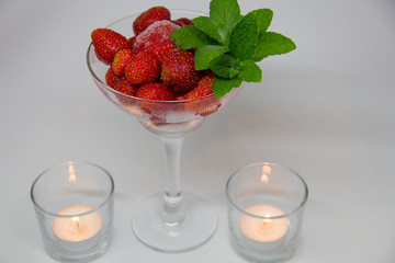 frozen strawberries with mint leaves in a glass and candles on a white background