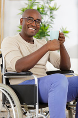 mature man in wheelchair drinking coffee near window indoors