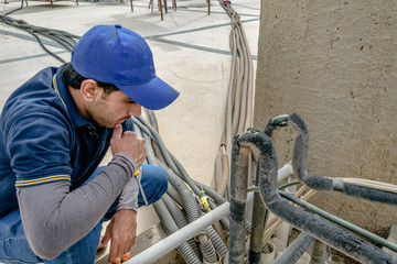 a professional electrician man is fixing the heavy unit of an air conditioner at the roof top of a building and wearing blue uniform and head cap