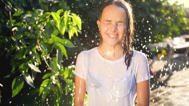 Slow motion closeup video of splashing bucket of water in teenage girls face at house backyard