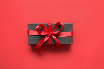 Black gift box wrapped with red ribbon on red surface.