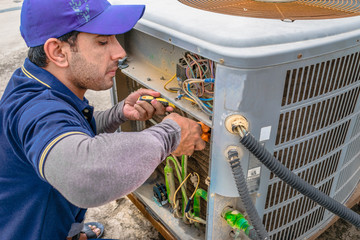 a professional electrician man is fixing the heavy unit of an air conditioner at the roof top of a building and wearing blue uniform and head cap - obrazy, fototapety, plakaty