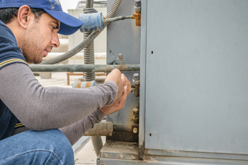 a professional electrician man is fixing the heavy unit of an air conditioner at the roof top of a building and wearing blue uniform and head cap