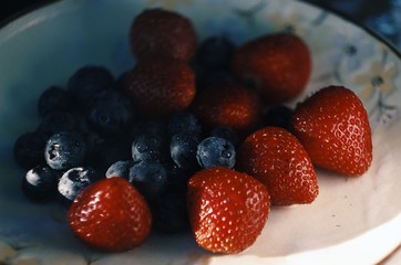 Blueberries and strawberries on ceramic plate. Wooden background. Fresh food vegan breakfast.
