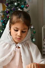 girl in a white cape near the new year tree