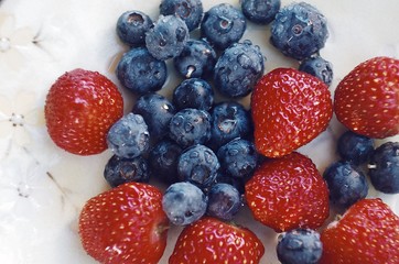 Blueberries and strawberries on ceramic plate. Wooden background. Fresh food vegan breakfast.