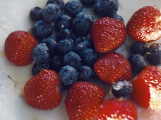 Blueberries and strawberries on ceramic plate. Wooden background. Fresh food vegan breakfast.