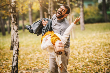 Playful laughing caucasian bearded father playing with his beloved daughter in park. Autumn time.