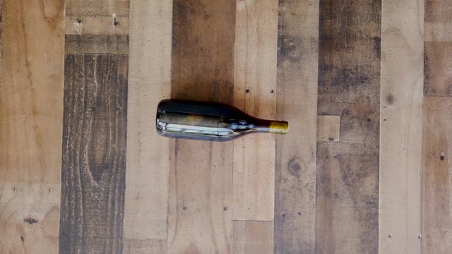 Red wine bottle spins on the wooden floor, flat lay, isolated, slow motion shot.