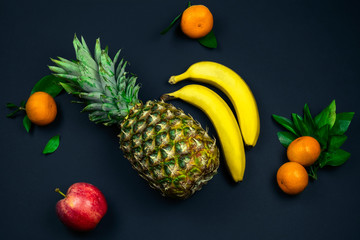 top view fresh tropical fruits layout pineapple,bananas, apple and tangerines on a black background