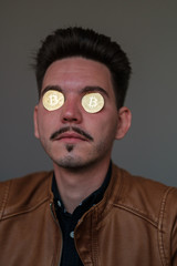 young man with bitcoins in the eye sockets on a dark background. portrait. close-up. emotions