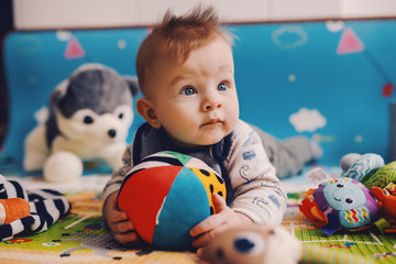 Adorable curious caucasian baby boy with big beautiful blue eyes lying on the floor on stomach,...