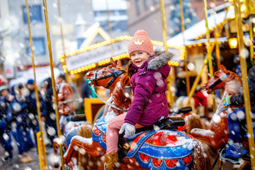Adorable little kid girl riding on a merry go round carousel horse at Christmas funfair or market,...