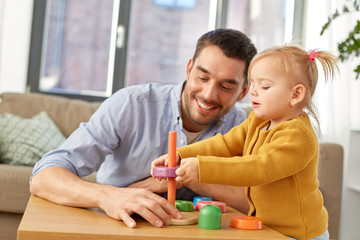 Obraz premium family, fatherhood and people concept - happy father and little baby daughter playing with pyramid toy at home