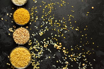 Different cereals are scattered on a dark table. Rice, wheat and other groats