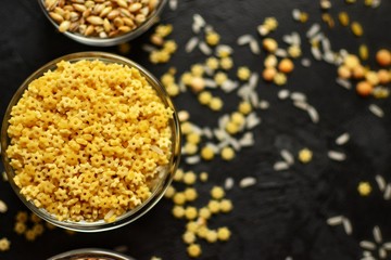 A variety of groats. Cereals in transparent bowls on a dark table background. Scattered grains