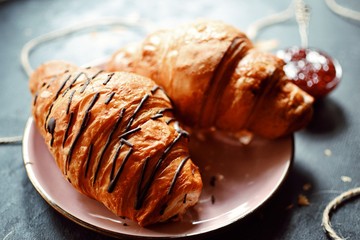 Croissants in a beautiful pink plate on a dark background. Fragrant croissants and raspberry jam in a bowl with a beautiful silver spoon.
