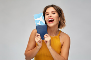 travel, tourism and vacation concept - happy laughing young woman in mustard yellow top with air ticket and passport over grey background