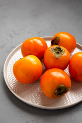 Raw Ripe Orange Persimmons on a plate over gray background, low angle view. Copy space.