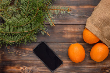 Oranges in a linen bag on a wooden background. Near fir branches and black smartphone. Christmas concert. Copy space