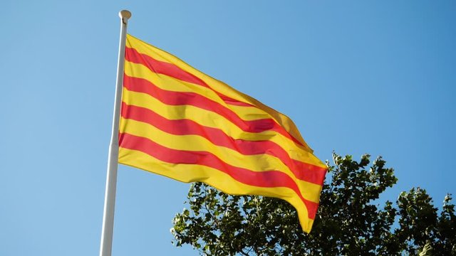 Close-up shot of the flag of Catalonia waving in the wind against blue sky. Barcelona. Spain. Slow motion. HD