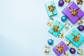 Flat lay background for celebration Christmas and New Year. Gift boxes are purple and turquoise with gold ribbons bows and confetti stars on a blue background. top view copy space.
