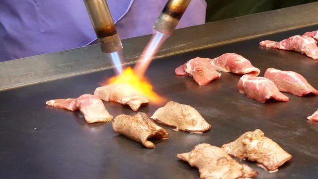 Chef using burnt torch prepares sushi. Cheff burns a slice of wagyu beef with blowtorch for make a sushi caramelize. 