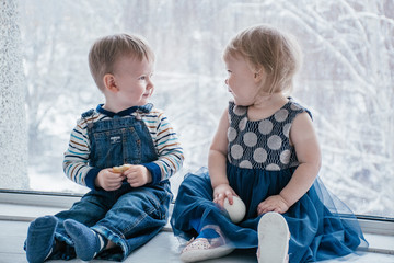 a boy and a girl are sitting at the winter window