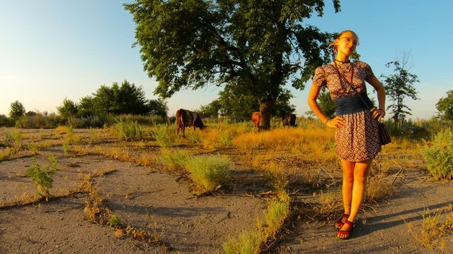 village cowgirl postures with hands in belt cows pasture on background sunset hot rural summer