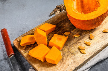 Raw pumpkin on a cutting Board, cut into cubes. Gray background. Tasty and healthy food. Pumpkin seeds. Vegan food