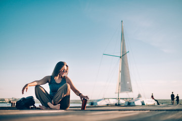A young woman is sitting on the pier by the yacht