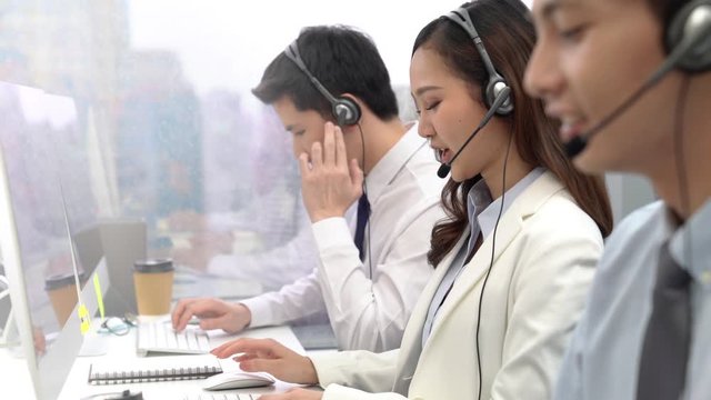 Beautiful customer service telemarketing Asian woman smiling at camera while working with team in call center office