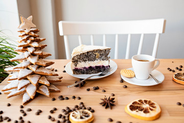 Christmas confectionery in bright interior with white chair and wooden table. Christmas tree mad from gingerbread and homemade poppy seed cake with cup of coffee. Christmas decoration.
