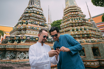 Men in a Buddhist temple read tourist information, look at a map on the phone.