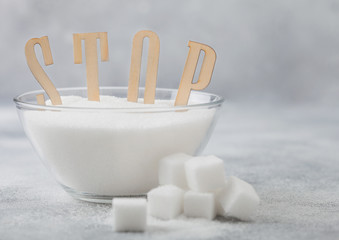 Glass bowl of natural white refined sugar with cubes on light table background with STOp letters. Unhealthy food concept.