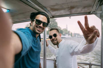 Young men sail on a ship and take a selfie against the background of a river in an Asian city