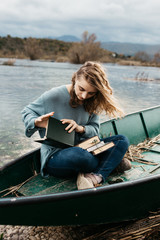 Portrait of young beautiful woman sitting on a boat and reading a book. She is bookworm and she choose between few books. 