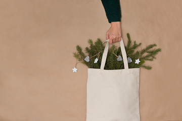 the female hand holds Cotton bag with pine branches and Christmas decor on a craft background. Zero...