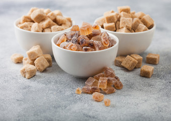 White ceramic bowl plates of natural brown unrefined and caramelized sugar cubes on light table background.