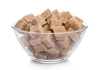 Glass bowl of natural brown sugar cubes on white background.