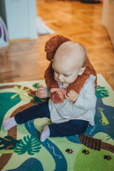 Fototapeta premium Adorable little Baby Girl is sitting on the carpet and playing with brown monkey toy