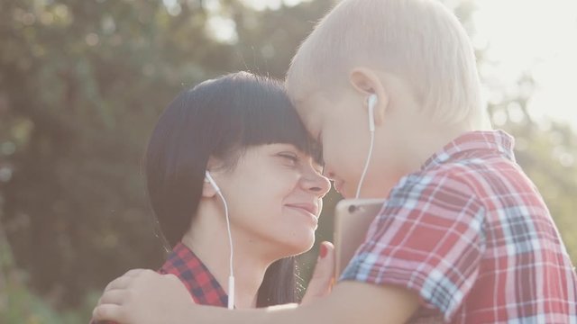 happy family funny nature slow motion video teamwork outdoors. Mom and son listen to music on smartphone in the same headphones for two . happy family mother woman lifestyle and son little boy spend