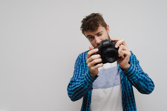 Young handsome hipster man with a camera in hand and a crazy creative face. Portrait of a young photographer, isolated on gray for copy space.