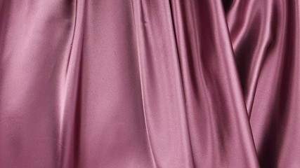 Dark pink satin fabric is draped with vertical soft folds, background