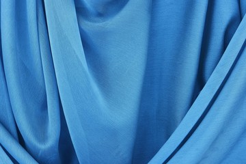 Natural silk of azur blue color is draped with soft pleats, background